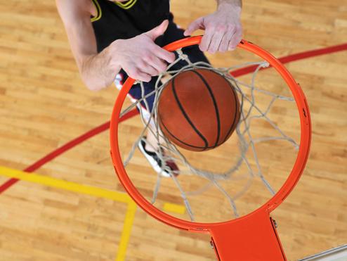 Basketballspieler zeigt den Ball beim Dunking durch den Korb von oben, umgeben von einem Holzfelddesign.