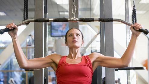Rückenfit im Remscheider Sportverein Frau in rotem Top trainiert an einer Kraftmaschine mit Latzuggriff im Fitnessstudio.