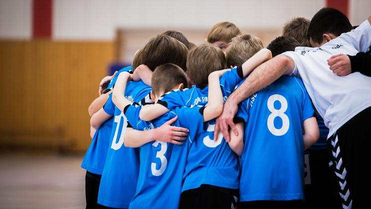 Gruppe junger Sportler in blauen Trikots umarmt sich in einer Halle vor dem Spiel.