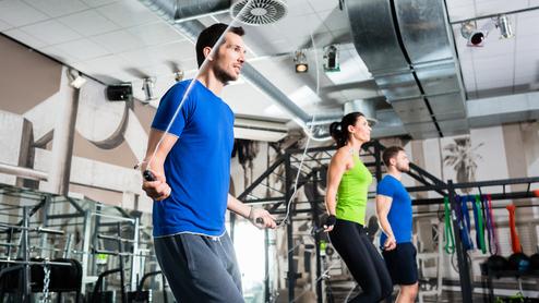 Drei Personen beim Seilspringen in einem modernen Fitnessstudio mit Geräten im Hintergrund.