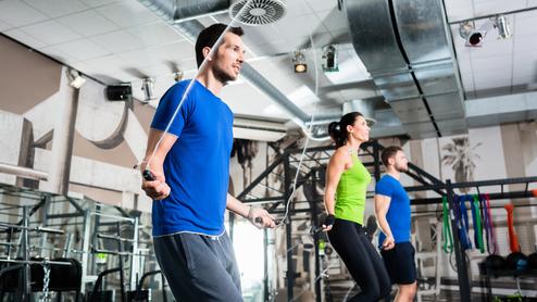 Drei Personen beim Seilspringen in einem modernen Fitnessstudio mit Geräten im Hintergrund.