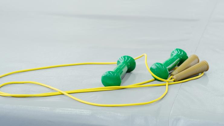 Grüne Dumbbells und ein Seil aus gelben Drähten liegen auf einer hellgrauen Trainingsmatte.