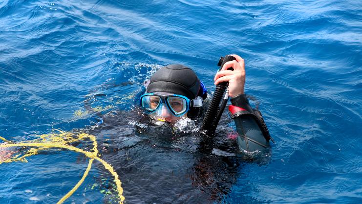 Taucherin mit Schnorchel und Maske im Wasser, umgeben von blauen Wellen und schwimmendem Gelbseil.